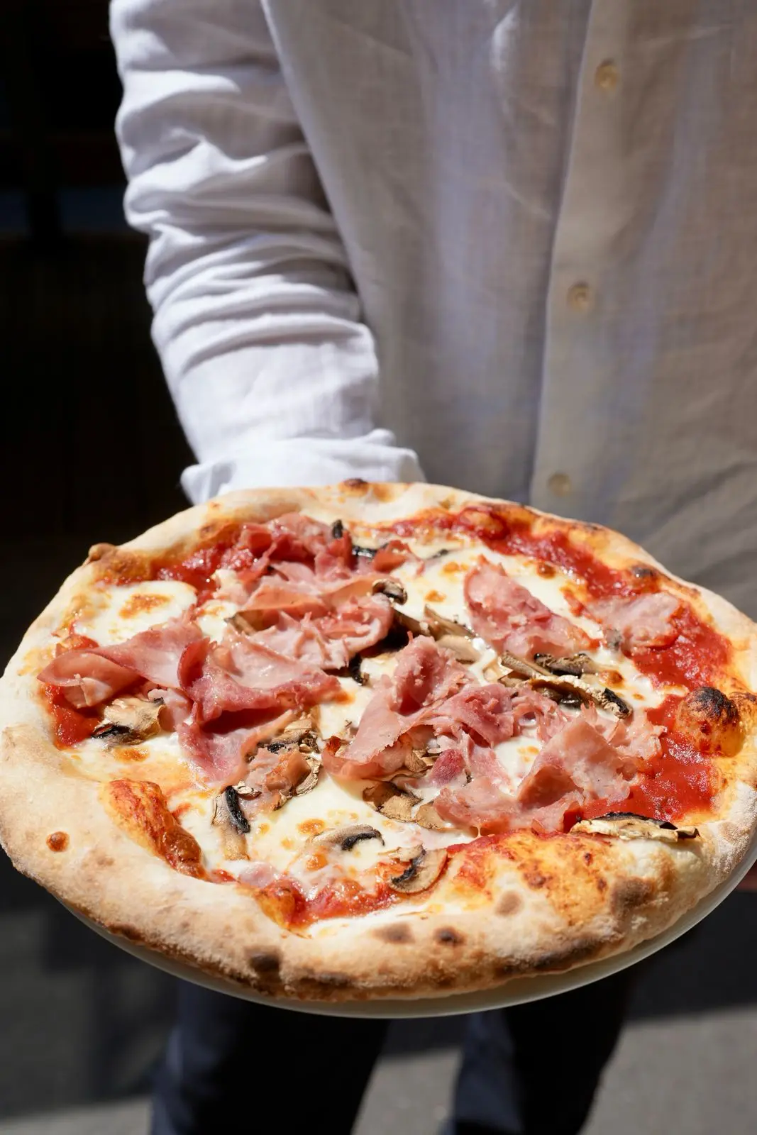 Une pizza jambon et champignons, présentée par un serveur