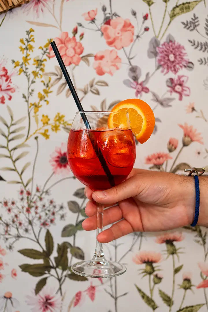 Un spritz tenu devant le papier peint fleuri