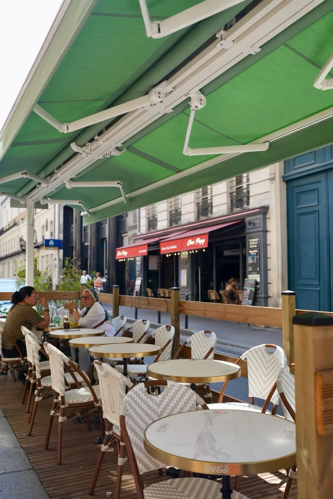 La terrasse sous les stores verts, des clients attablés