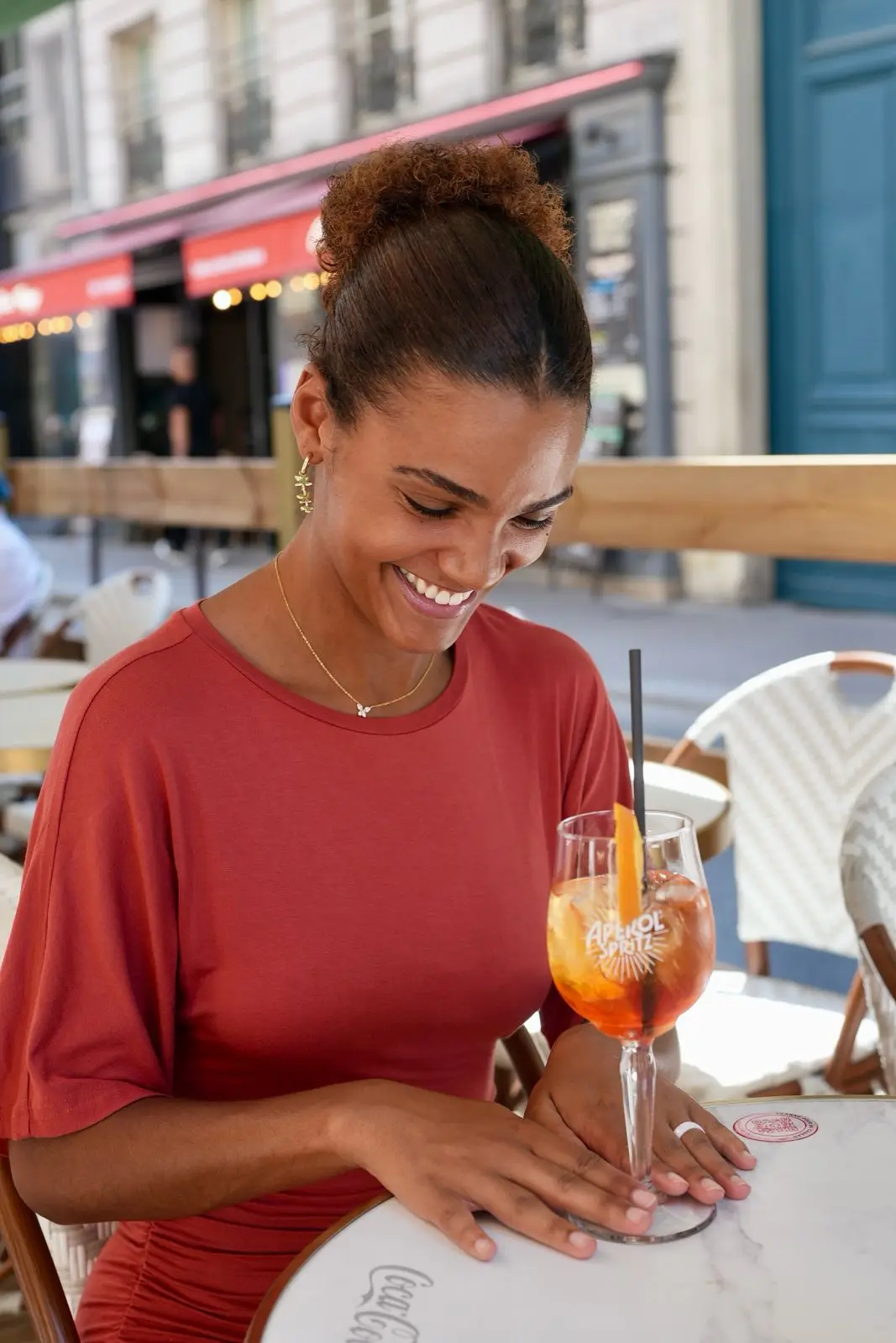 Une cliente sourit, un spritz à la main, en terrasse
